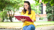 Beautiful female college student reading a book on a bench in a park