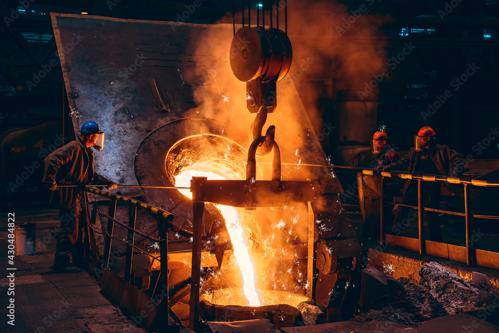 Pouring bright liquid iron or metal with sparks into container in steel mill or workshop blast furnace foundry. Metal casting process in metallurgical plant. - obrazy, fototapety, plakaty 