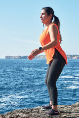 Poster - Hispanic female in a sports outfit working out and doing exercises on the beach near rocky cliffs