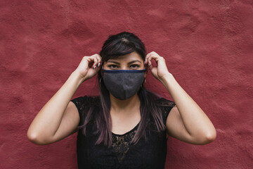 Young Ecuadorian female wearing a fabric face mask on burgundy wall background