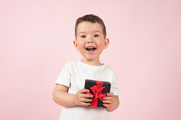 Wall Mural - Close-up portrait of happy little boy with wrapped present on pink background