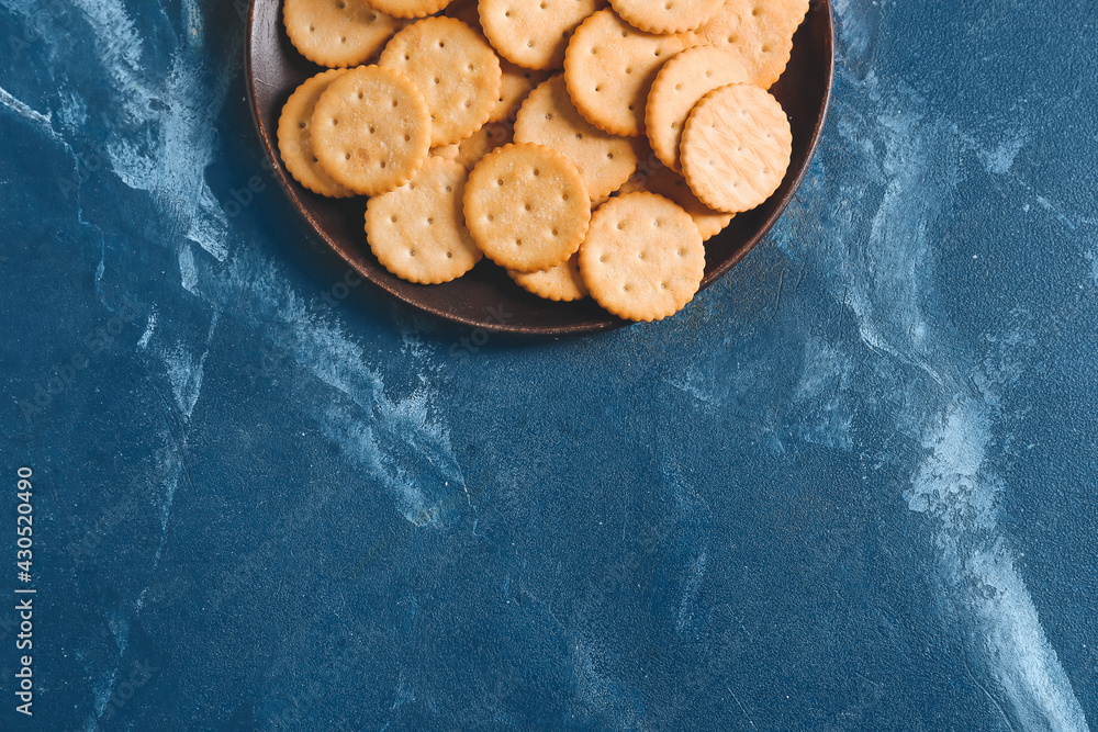 Plate with tasty crackers on color background