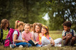 © liderina - Large group of school kids having fun in nature. Little girl reading book to her friends.