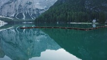Most beautiful Lago di Braies also known Pragser Wildsee. Dolomites, Italy. Flying out over the calm emerald green water surface and boats in a raw.