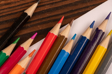 Colorful pencils and white sheets of paper on a wooden table.