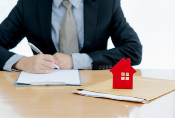 A House on document envelope with man signing purchase documents in background. while hand complete the insurance policy, rental documents and loan document. concept guy buying new house