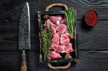 raw diced pork cubs meat with spices in a rustic tray. black wooden background. top view