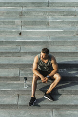 Wall Mural - Confident athletic man sitting on concrete stairs after fitness workout outdoors