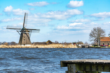 A boat dock in the rough water of lake De Rottemeren with the windmill De Korenmolen in the background on a sunny but stormy day 2