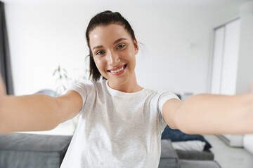 European brunette woman smiling while taking selfie photo at home