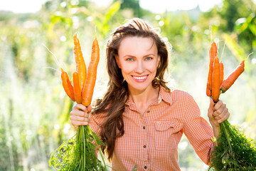 Wall Mural - Beautiful farmer woman with carrots, outdoor shot