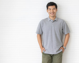 Portrait close up shot of handsome asian male model with short black hair wearing gray polo shirt stand smiling in front of white background