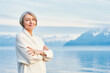 Outdoor portrait of beautiful middle age woman posing next to winter lake, wearing white coat