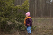 © Татьяна Толстая - a little girl in a purple jacket and an orange scarf stands and looks at a coniferous tree