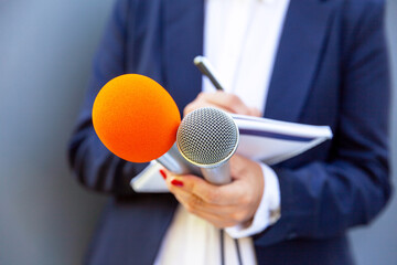 Wall Mural - Microphone in focus, female journalist at press conference writing notes. Public relations (PR) concept.
