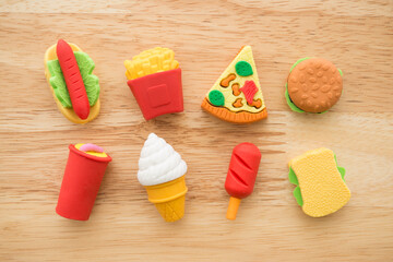 Flat lay of cute various fast food products and drinks eraser toy set on wooden background minimal style. Kid learning, development and funny play by small eraser toy in school accessories.