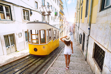 woman tourist walking in narrow streets of lisbon city old town. famous retro yellow funicular tram 