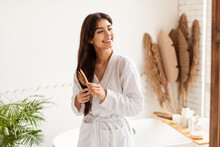Brunette Woman Brushing Hair With Wooden Hairbrush In Modern Bathroom