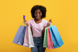 Fototapeta Mapy - Overjoyed african american lady with shopping bags and credit card smiling over yellow background, studio shot