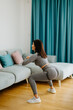 © shevtsovy - Athletic woman sports workout at home, squats. Home workout. Slim female stretching at home and weight loss workout in a living room.