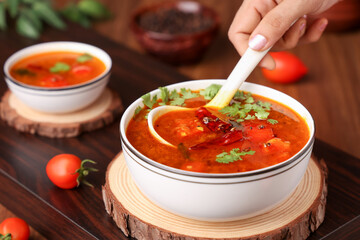 Woman hand serving tomato rasam curry hot spicy soup South Indian cuisine use Indian spices, tamarind , chili, cumin. Traditional vegetarian dish rice onam sadhya Kerala, Tamil Nadu, India Sri Lanka.