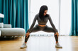 © shevtsovy - Young attractive woman practicing yoga at home, legs stretching practice. Relaxation and legs stretching in living room. Beautiful fitness female wearing yoga pants gymnastics morning routine.
