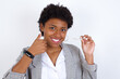 © Roquillo - African American businesswoman with curly bushy hair wears  formal clothes holding an invisible braces aligner and rising thumb up, recommending this new treatment. Dental healthcare concept.