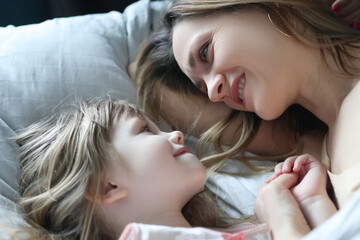 Mom and daughter looking at each other and lying in bed