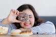 Closeup shot of delicious chocolate donut decorated with colorful sugar sprinkles in Asian young happy beautiful long black hair oversized fat female model hand who smile look through doughnut hole