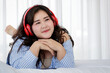 © Bangkok Click Studio - Asian young happy calm fat overweight woman lay down with happy smiling deep emotion peacefully while listening to music from big red earphones use playlist from black tablet at home in bedroom