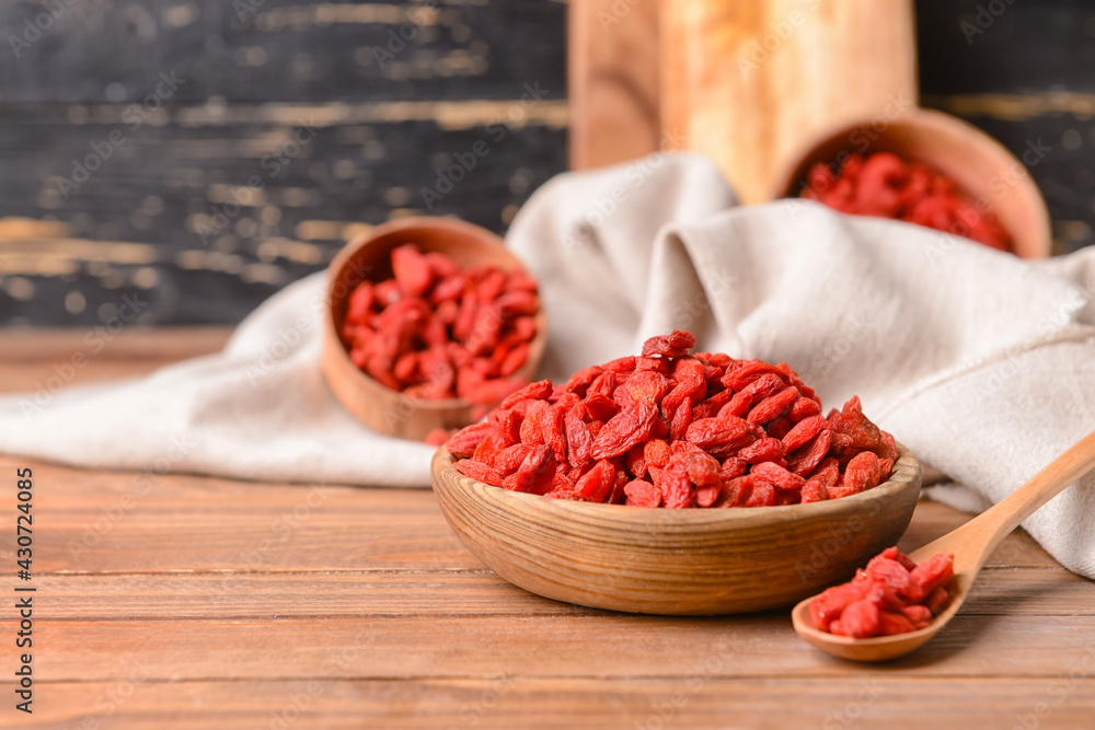 Bowl and spoon with dried goji berries on wooden background