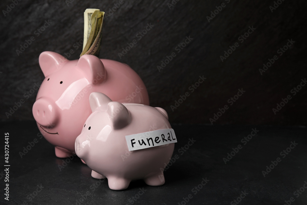 Piggy banks and word FUNERAL on dark background