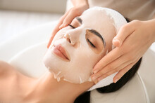 Cosmetologist applying sheet mask on woman's face in beauty salon