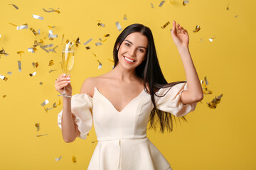 Wall Mural - Beautiful woman with glass of champagne and falling confetti on color background