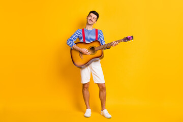 Wall Mural - Full size photo of young handsome happy positive smiling dreamy man playing guitar isolated on yellow color background