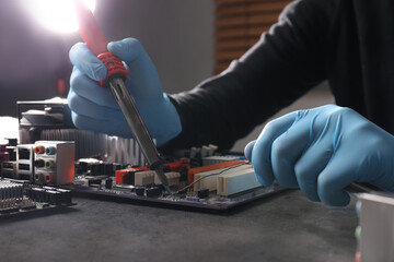 Wall Mural - Technician repairing electronic circuit board with soldering iron at table, closeup