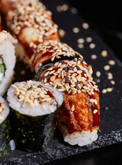 Wall Mural - Sushi sashimi and maki sprinkled with sesame seeds on a stone plate on a dark background.