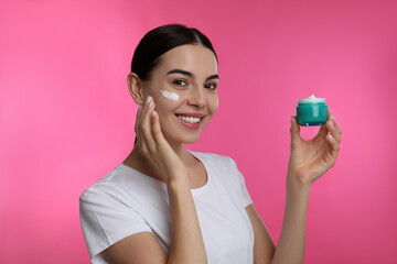 Canvas Print - Young woman applying facial cream on pink background