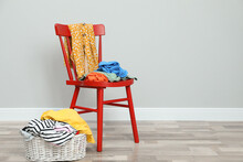 Red Chair And Wicker Basket With Different Clothes Near Grey Wall, Space For Text