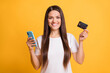 © deagreez - Photo portrait of happy woman smiling using mobile phone keeping plastic bank card isolated on vibrant yellow color background