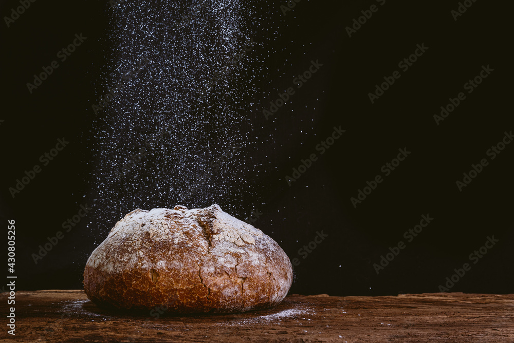 rustic and golden round loaf of fresh whole grain bread on dark black ...