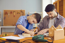 Concentrated Father And Son Building Wooden Birdhouse Spend Time Together. Caucasian Family At Carpentry Workshop. Home Leisure Activity, Educational Entertainment And Parent Pastime With Children