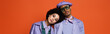 curly woman in purple jacket leaning on model in beret and sunglasses isolated on orange, banner