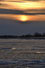 A Landscape View Of The Frozen Sea During Ice Drift In Spring With Dramatic Sky And With Reflections In Melt Water In The Evening At Sunset. In The Distance, The Black Strip Of The Island.