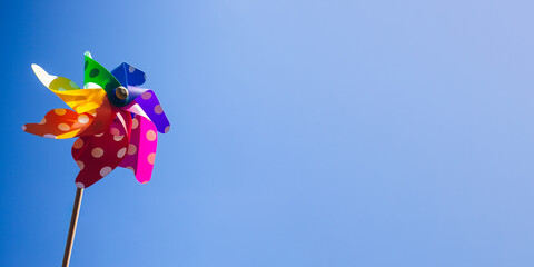 Vibrant rainbow coloured pinwheel on blue sky expressing freedom and sustainable wind power.