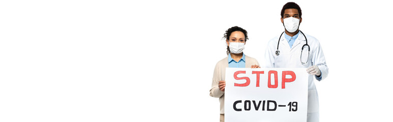 Wall Mural - African american patient and doctor in medical masks holding placard with stop covid-2019 lettering isolated on white, banner