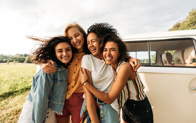 four happy female friends laughing together standing in front of a van. women enjoying summer road t