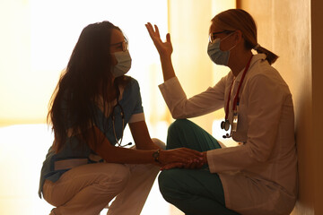 Two tired doctors in medical masks in corridor of hospital