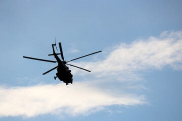 Military helicopter silhouette in flight on background of blue sky and white clouds. Bottom view, air transportation concept