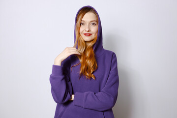 A redhead woman in a purple hoodie adjusts the hood. White background